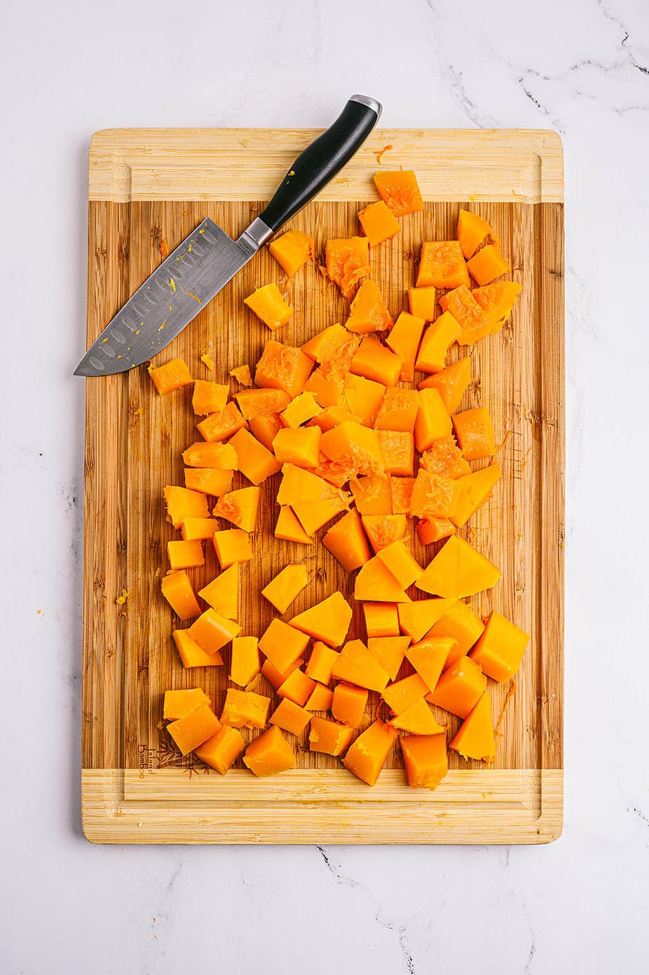 Overhead photo of cubed and cut butternut squash on a wooden cutting board with a chef's knife off to the side.