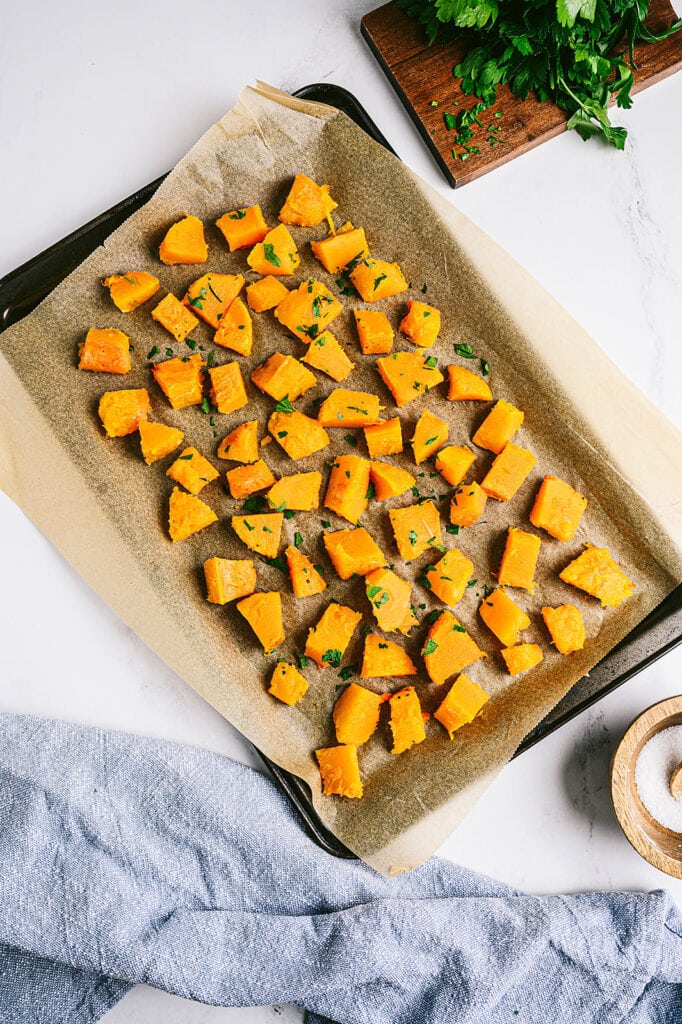 Overhead photo of cooked and cubed butternut squash on a parchment lined baking sheet.  