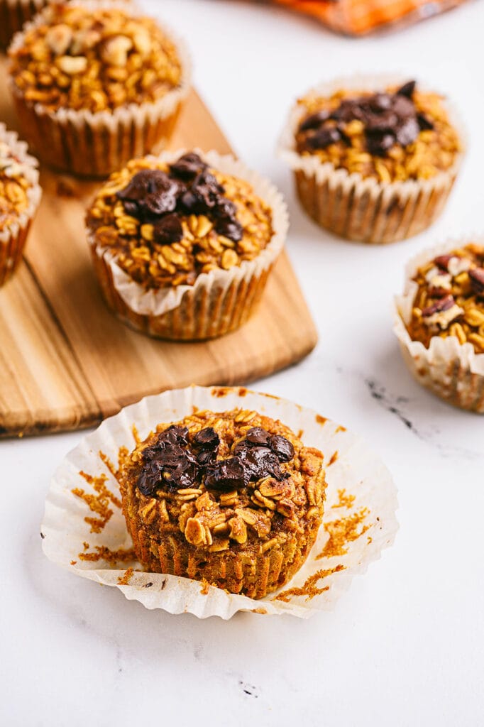 High angle photo of pumpkin oatmeal muffins with various toppings, on a cutting board and white counter.