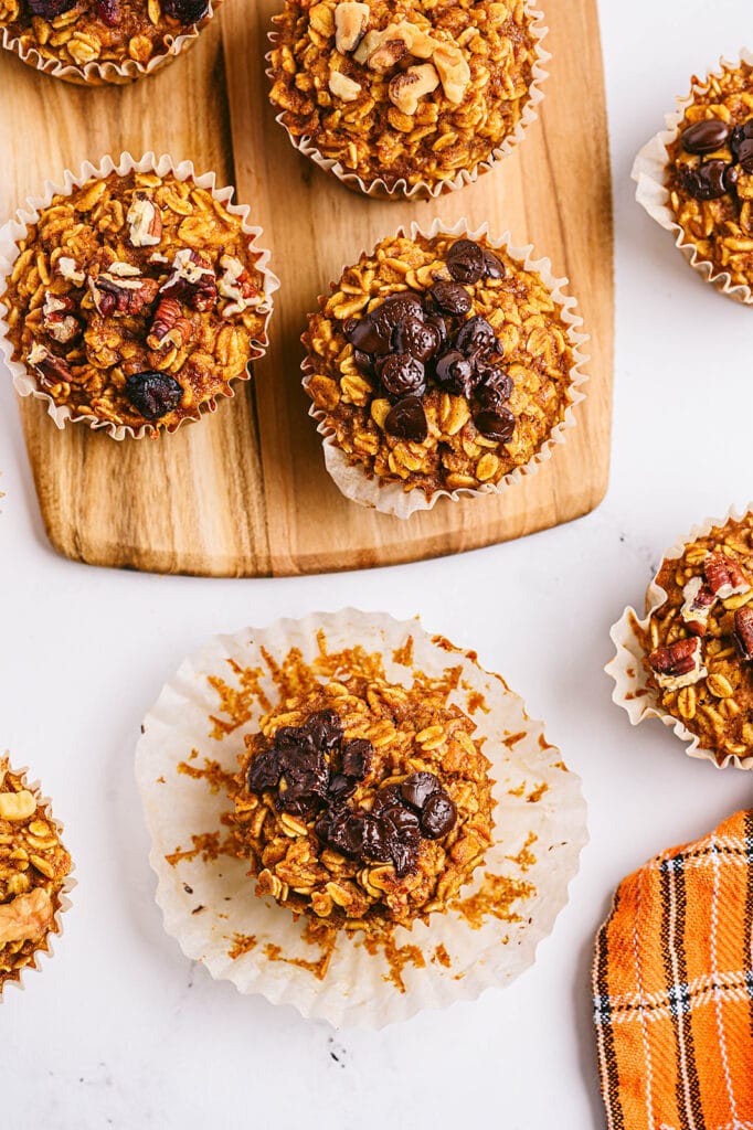Overhead image: pumpkin oatmeal muffins with chocolate chips and/or nuts on top. Some are on a white counter top, while others are on a wooden cutting board.