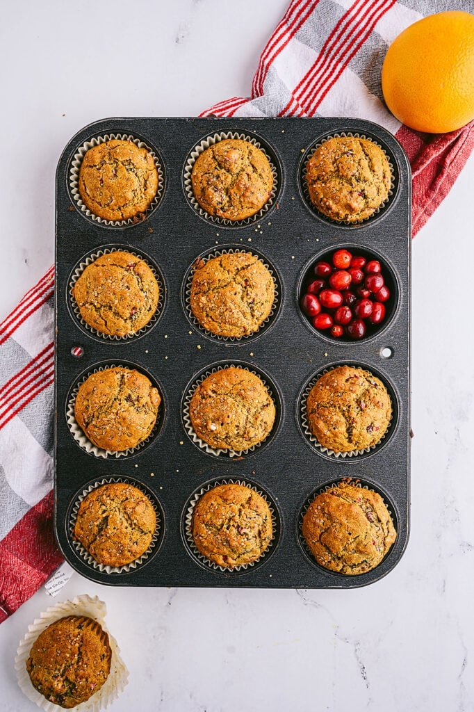 Overhead shot of a muffin tin of Cranberry Orange Muffins.  One of the muffins is replaced with fresh cranberries. 