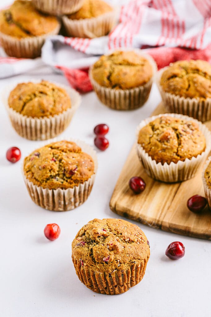 A dozen gluten free cranberry orange muffins with red and white kitchen towels and fresh cranberries strewn about. 