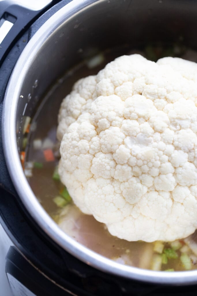 Overhead image: Head of cauliflower on top of chicken and dumplings ingredients, in the Instant Pot.
