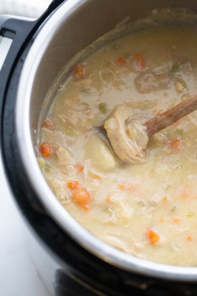 Overhead image: Chicken and dumpling soup in an instant pot with a wooden spoon.
