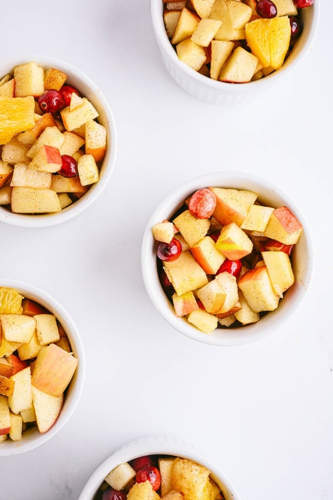 Overhead shot of four white ramekins with diced up fruit for a holiday crisp recipe