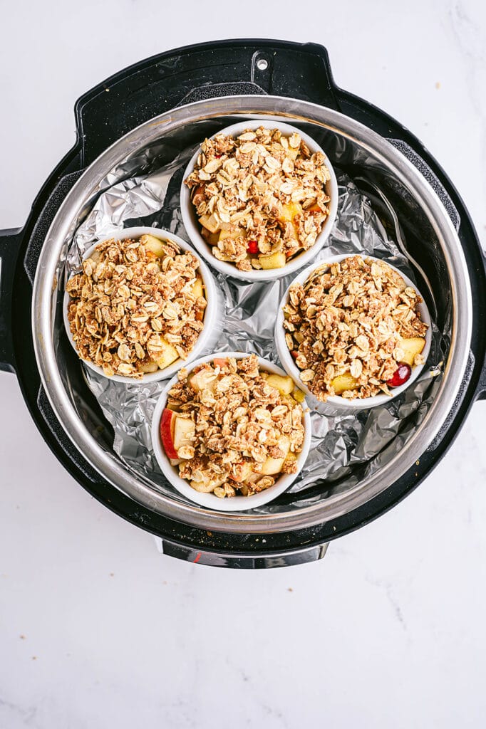 Overhead shot of four white ramekins with pear apple cranberry crisp topped with oats in an Instant Pot.