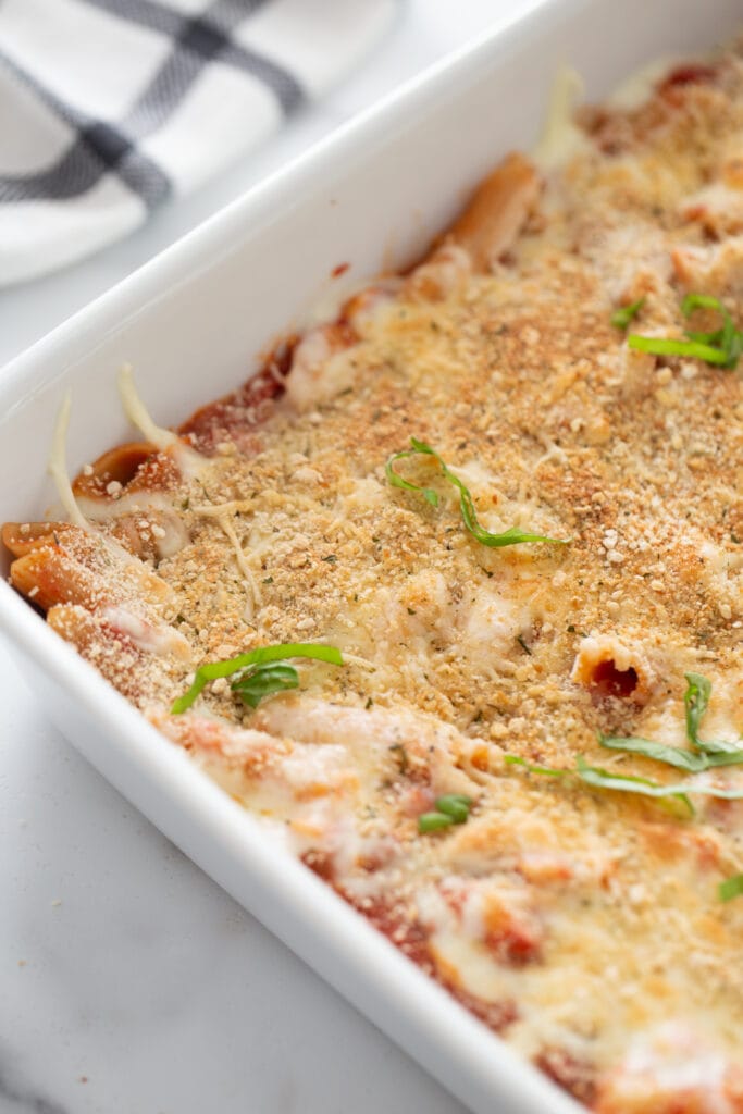 High angle photo of baked chicken parmesan pasta in a white casserole dish, garnished with fresh basil.