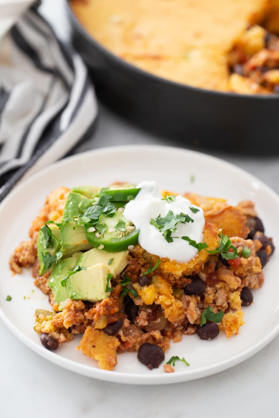 A plate of chili topped with cornbread, avocado slices, and Greek yogurt. 