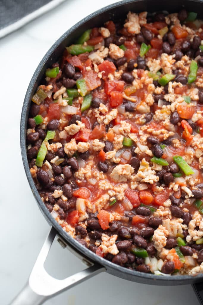 Overhead image: beans, diced tomatoes, ground meat, and diced peppers in a skillet .