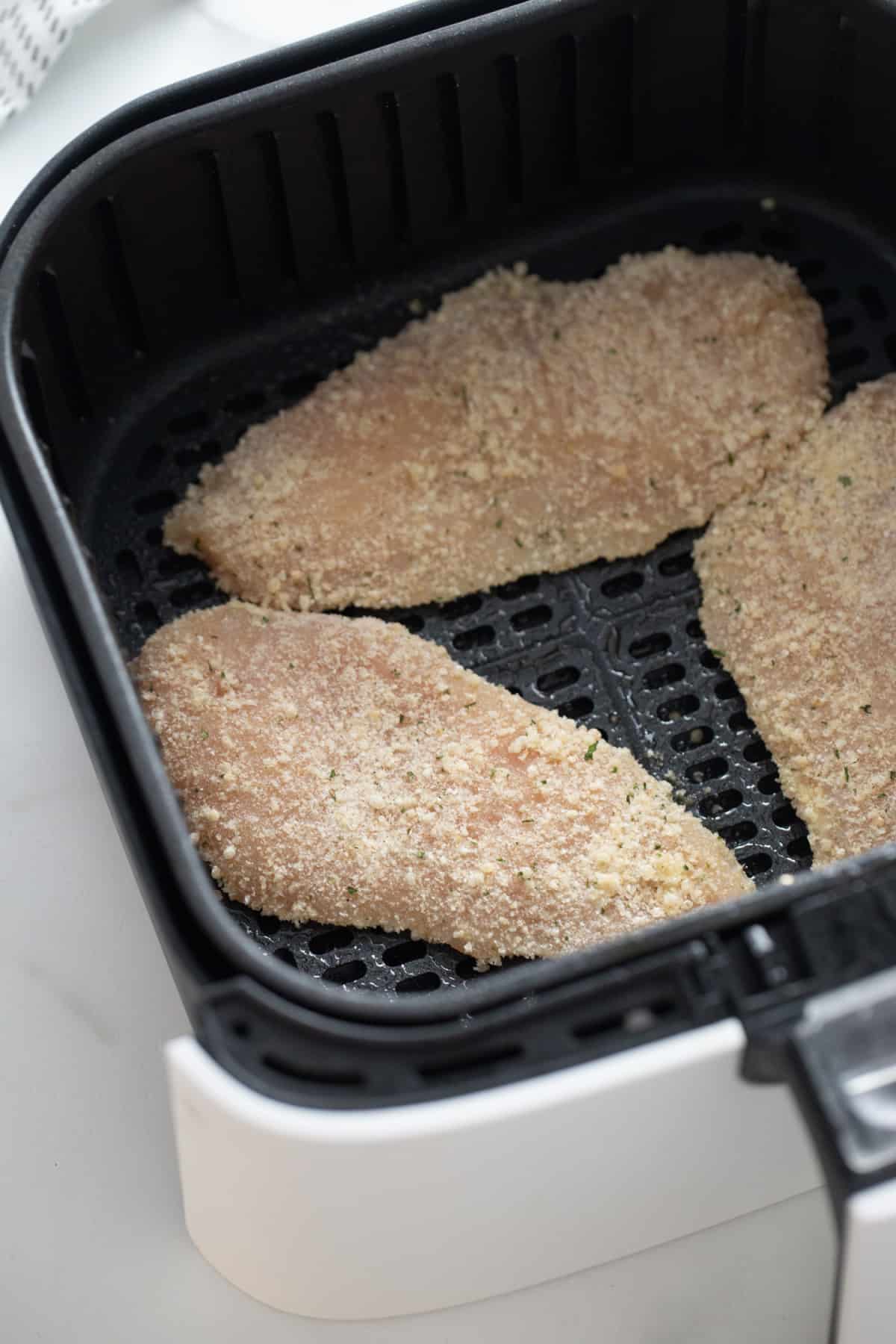 Three air fryer chicken breasts in an air fryer basket 