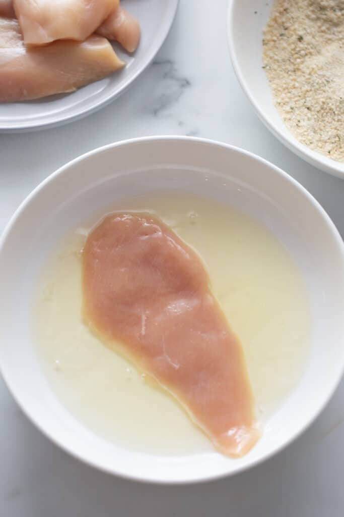 Overhead shot of a piece of thin chicken breast in a bowl of egg whites 
