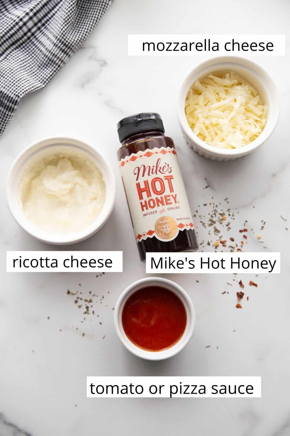Toppings for hot honey pizza: sauce, ricotta cheese, mozzarella cheese, and a bottle of Mike's hot honey. 