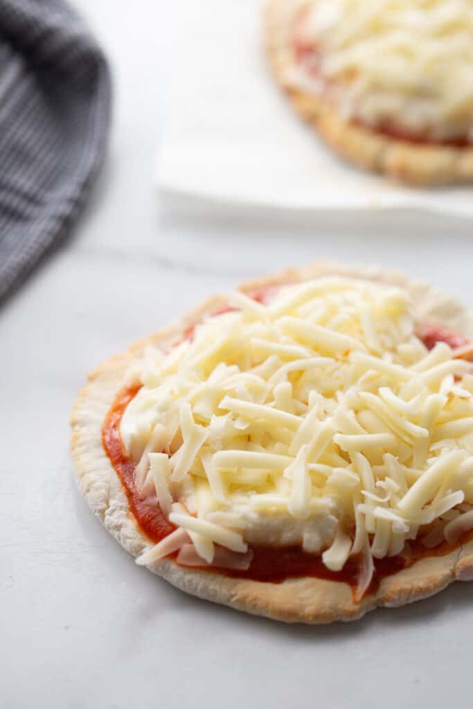 A small personal pizza topped with sauce, ricotta and mozzarella cheese sitting on a white counter. 