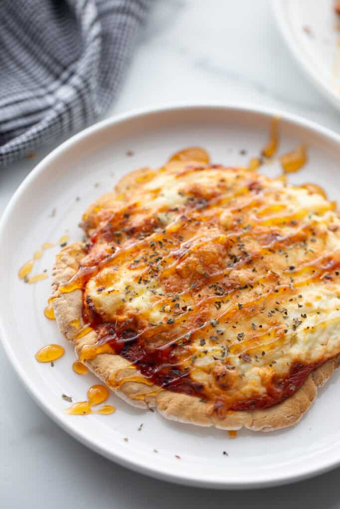 A personal pizza with melted cheese, ricotta, and hot honey drizzled over top. 