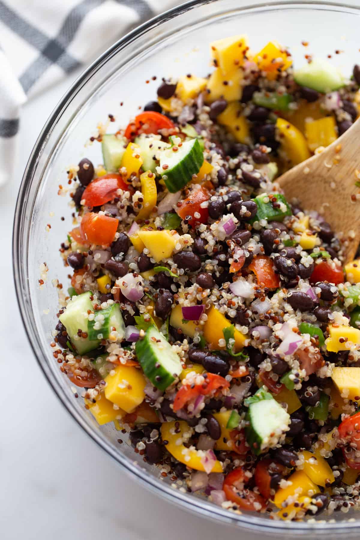 Chopped veggies, black beans, mangoes, and cooked quinoa in a bowl all mixed together.