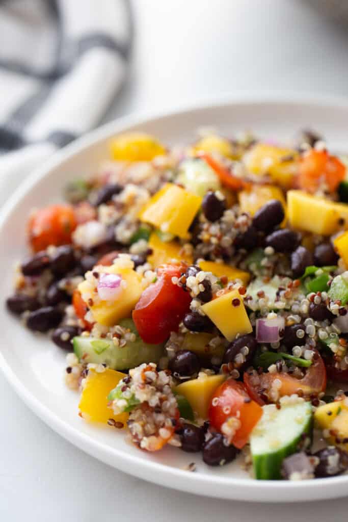 Close up photo of quinoa and black bean salad on a white plate.  There are chopped veggies, cooked quinoa, and black beans all mixed together.