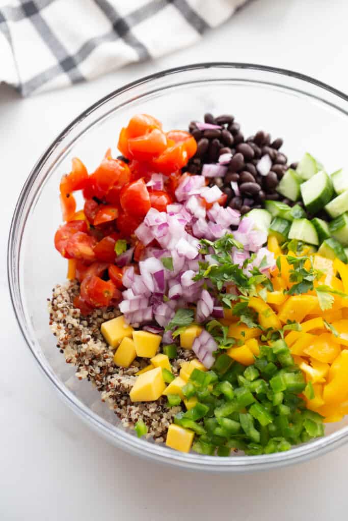 Diced veggies and cooked quinoa separated by ingredient in a clear bowl