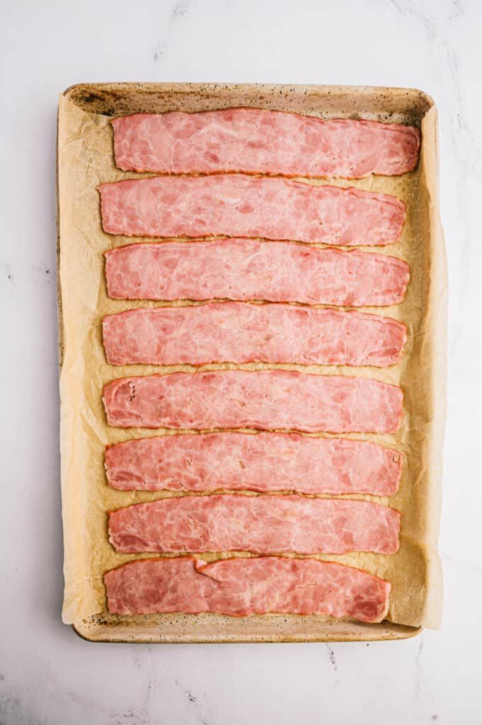 Parchment lined baking sheet with uncooked turkey bacon lined up horizontally, ready for the oven.
