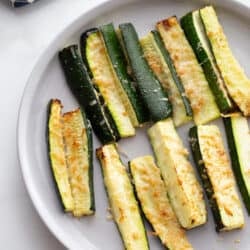 A white plate with air fryer zucchini topped with crispy cheese
