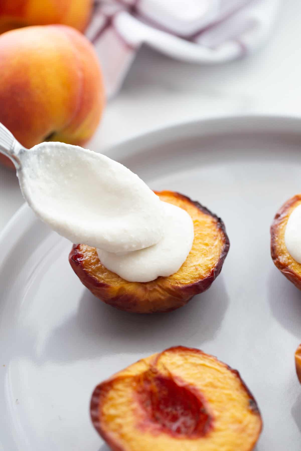 Air fried peaches on a plate - one has whipped ricotta being spooned on top
