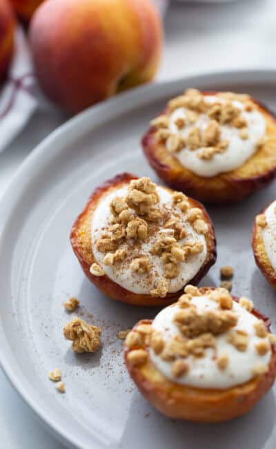 Three air fried peach halves on a white plate topped with whipped ricotta cinnamon and granola