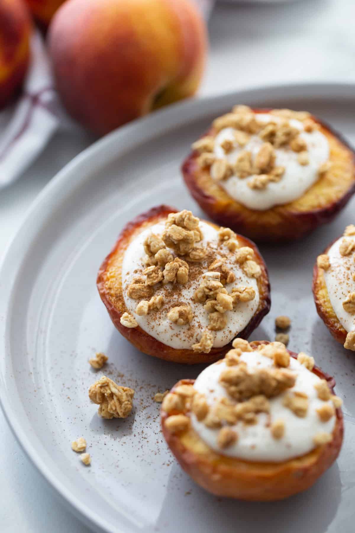 Three air fried peach halves on a white plate topped with whipped ricotta cinnamon and granola
