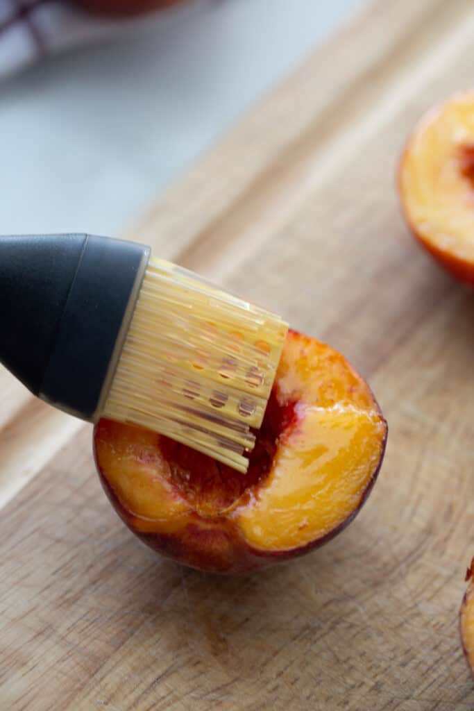 Half of a peach with coconut oil being brushed on top