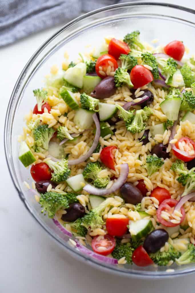 Orzo salad ingredients mixed up in a glass bowl.