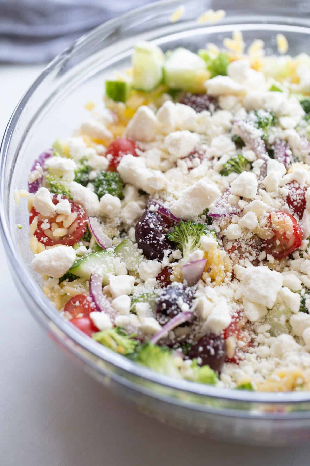 Gluten free orzo salad in a glass bowl, topped with feta cheese