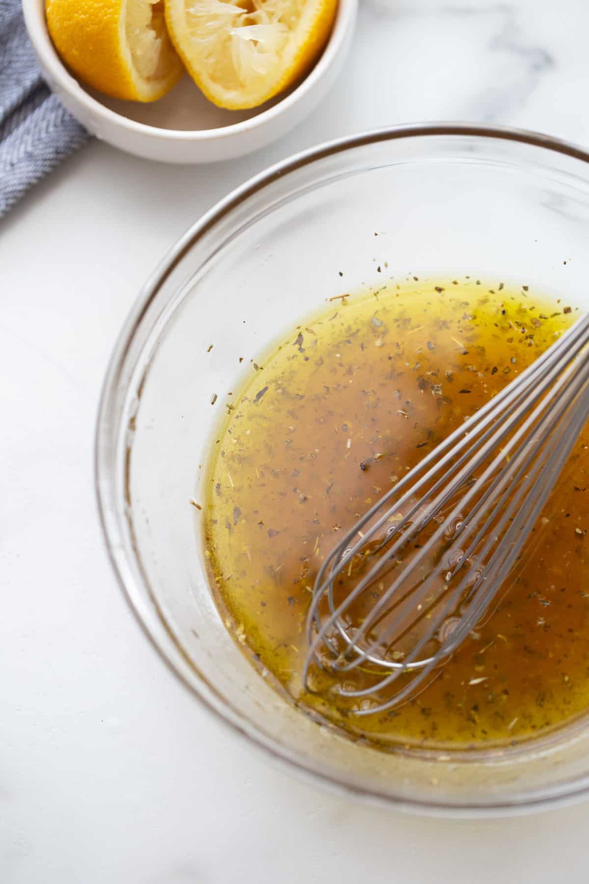 Glass bowl of homemade dressing with a metal whisk.