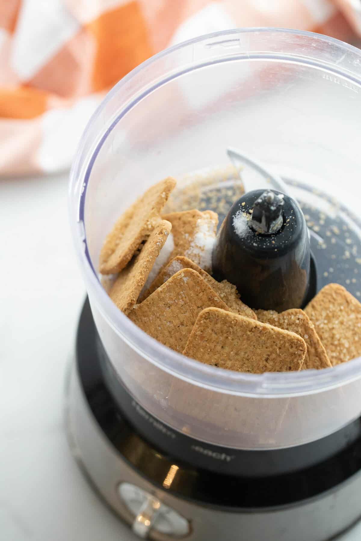 An overhead shot of a food processor with gluten free graham crackers and sugar inside ready to make a crust. 