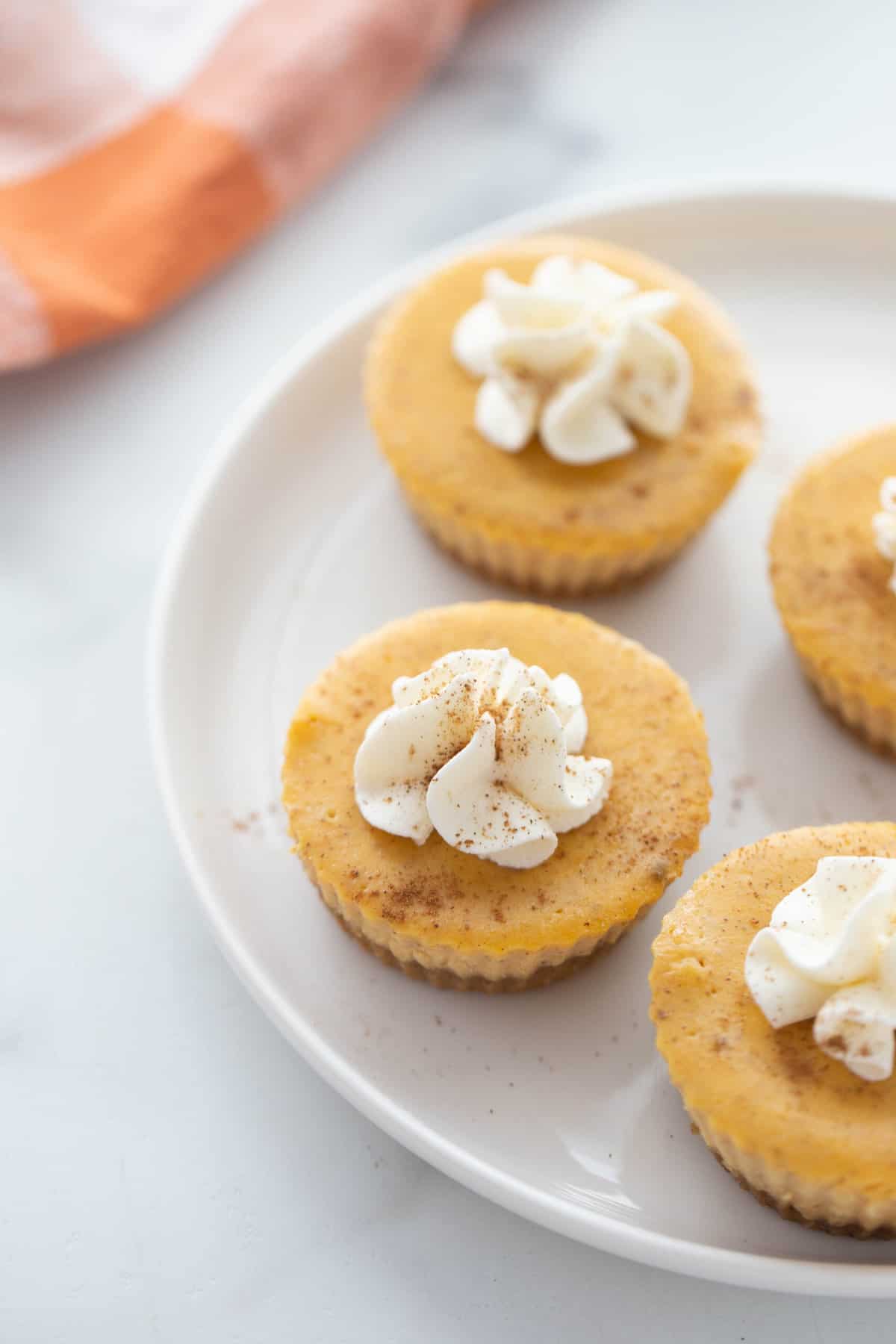 A plate with 4 healthy pumpkin cheesecake bites topped with whipped cream. 