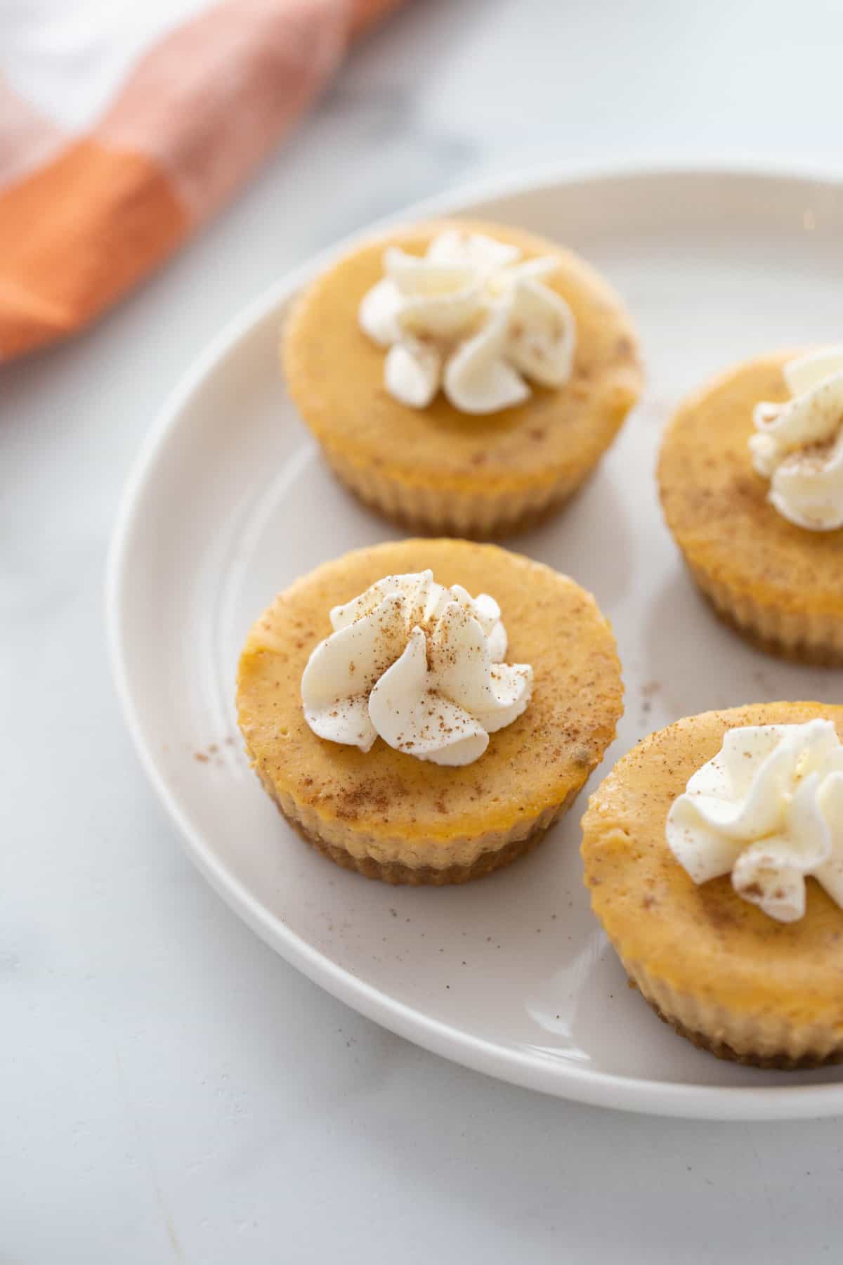 A plate of 4 pumpkin cheesecakes with graham cracker crust with whipped topping. 