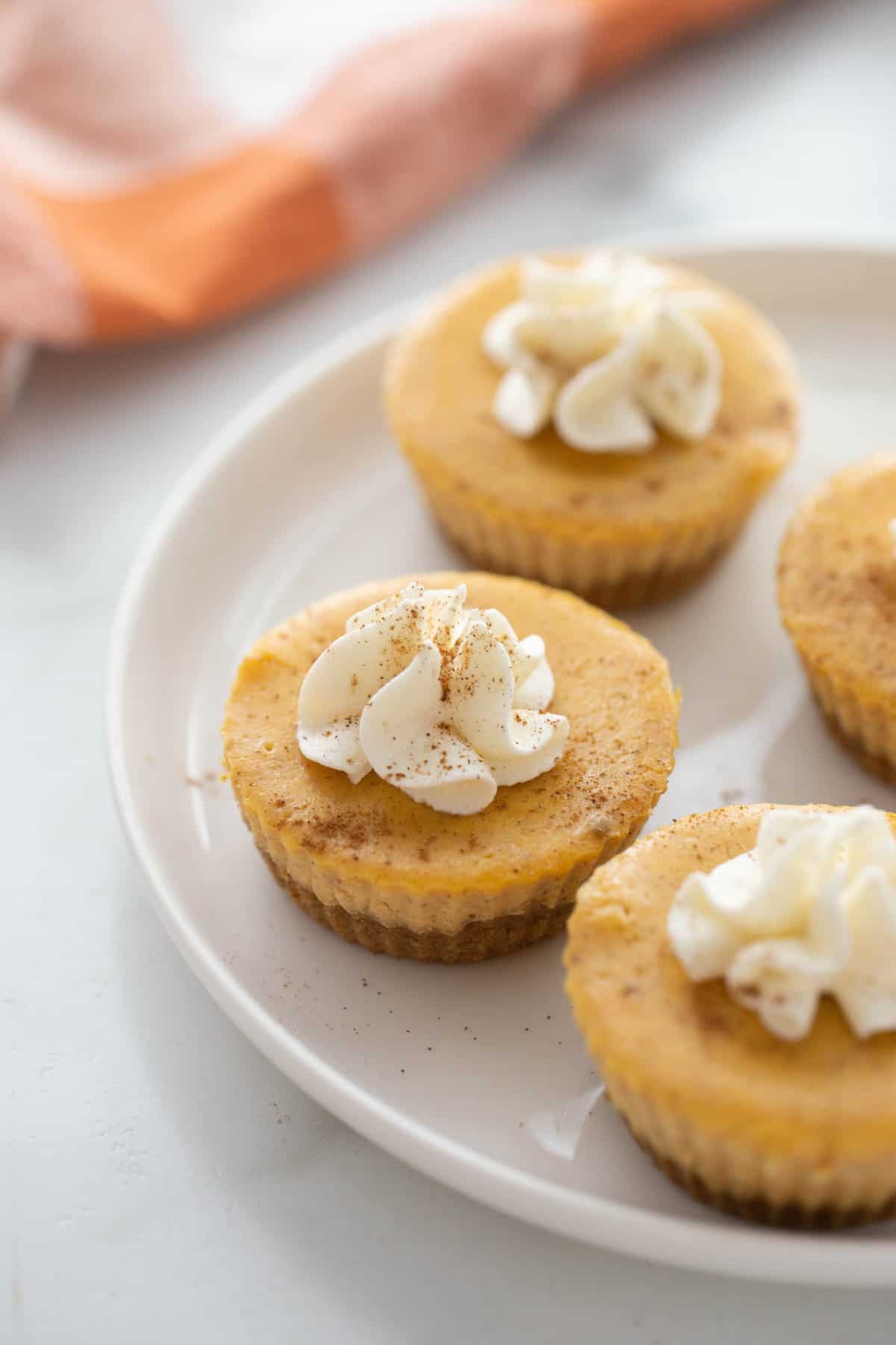 A plate of mini pumpkin cheesecakes topped with whipped cream. 
