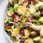 A plate of air fried Brussels sprouts topped with hot honey, bacon, and parmesan cheese.