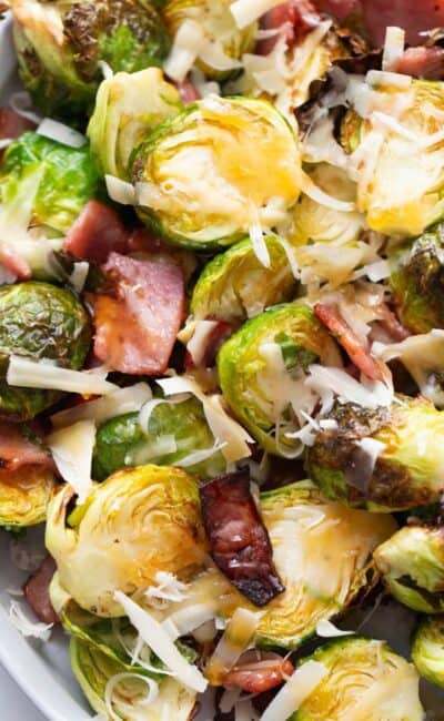 A plate of air fried Brussels sprouts topped with hot honey, bacon, and parmesan cheese.