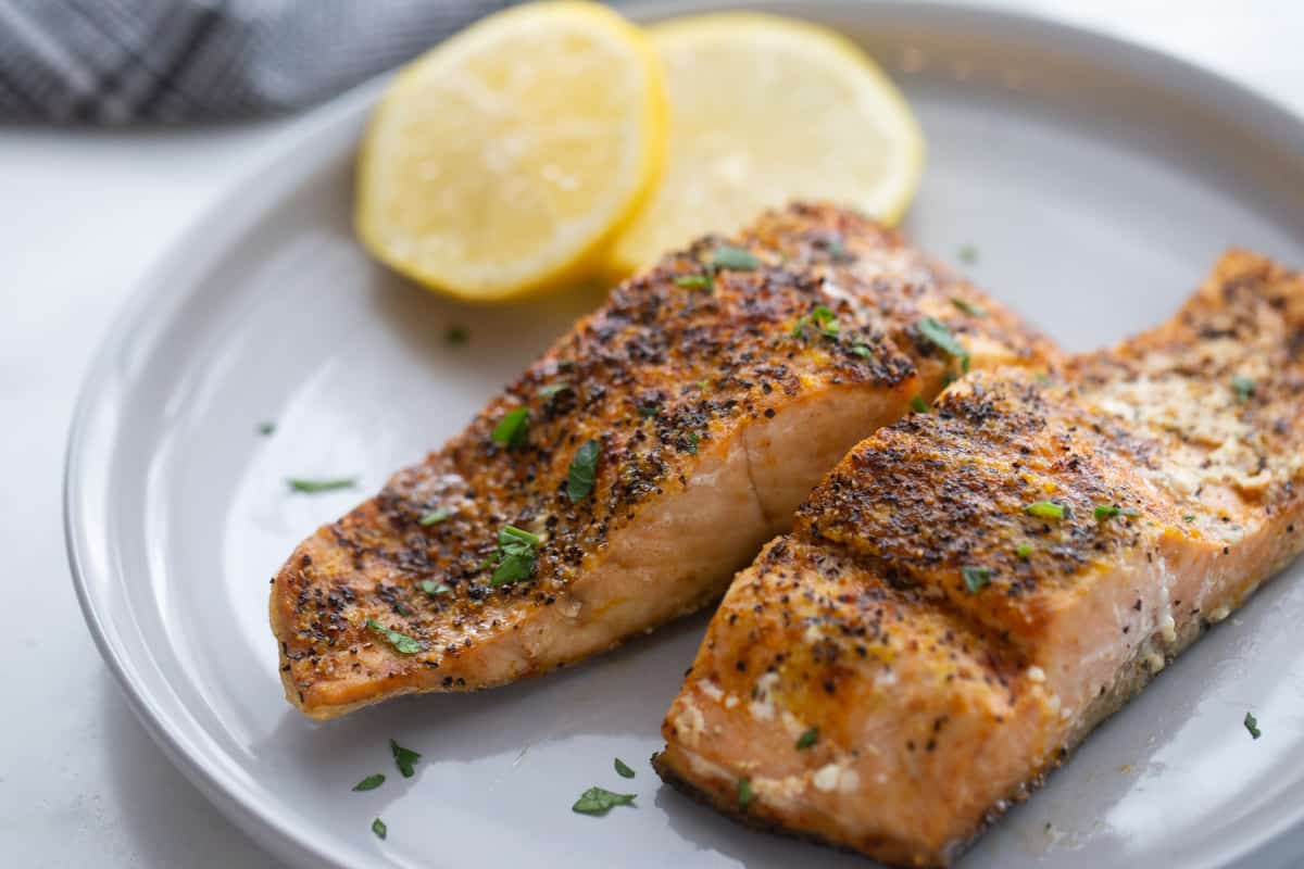 A plate with two pieces of Air Fryer Salmon cooked with seasonings and sliced lemons. 