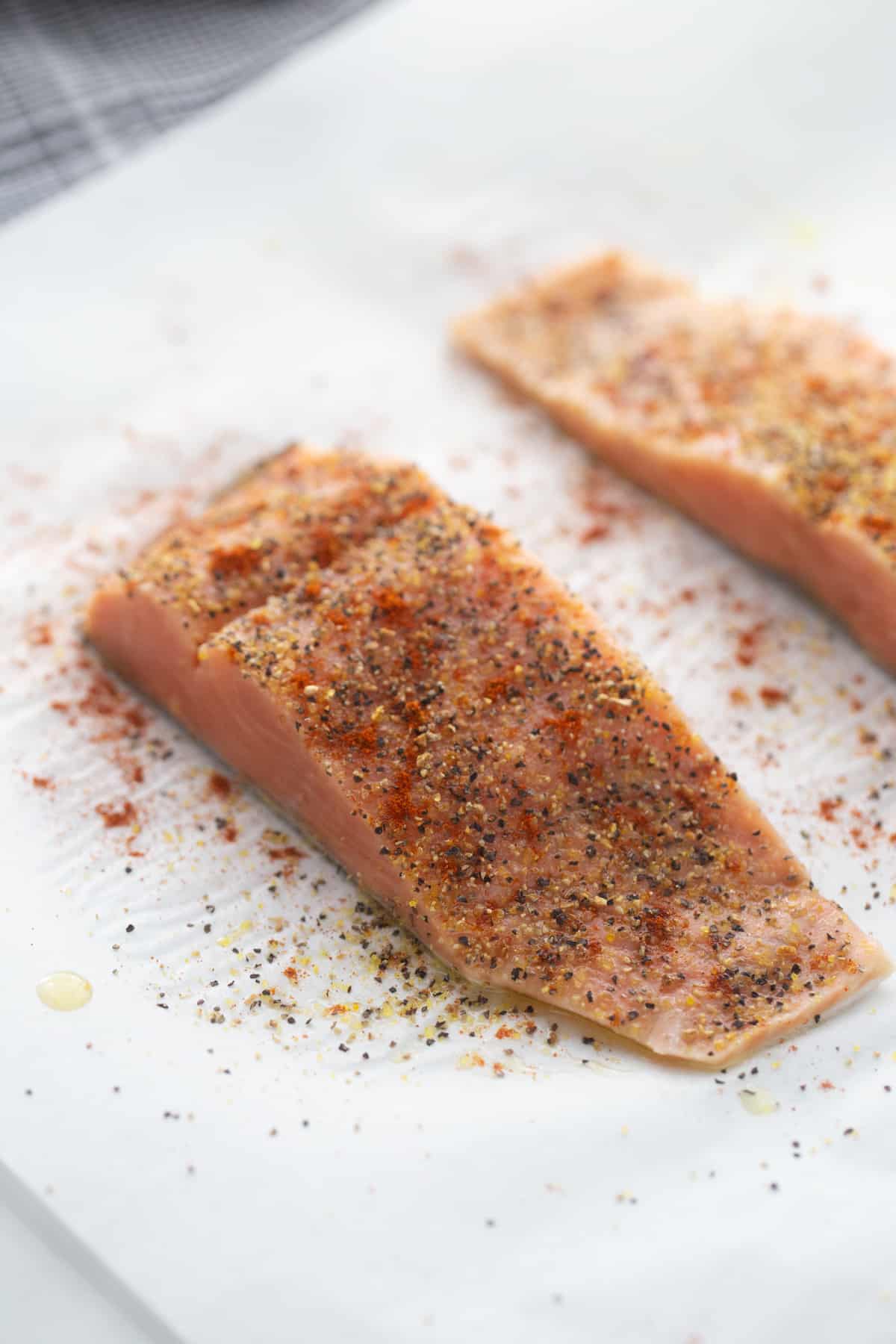Salmon on parchment paper topped with lemon pepper seasoning. 