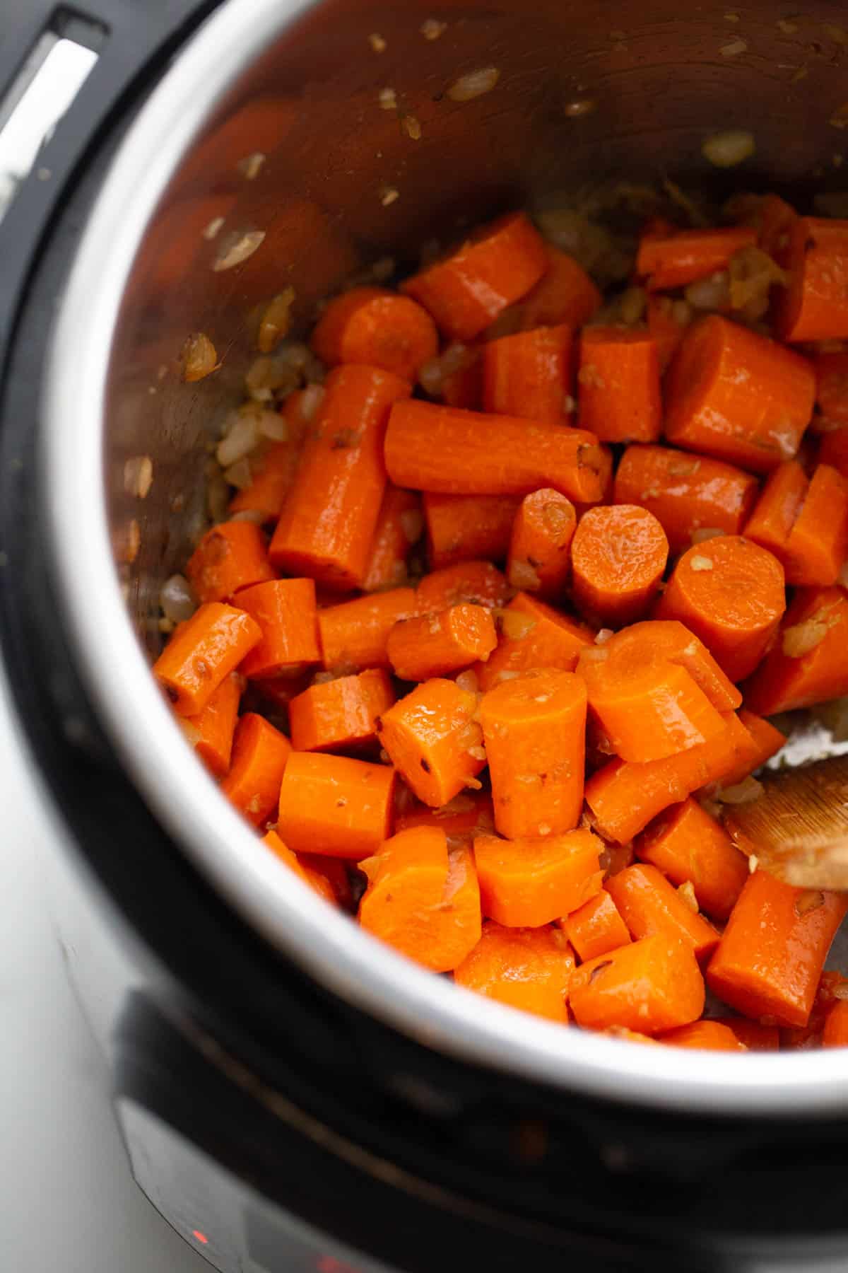 Roughly chopped carrots sautéing in an instant pot for creamy carrot ginger soup. 