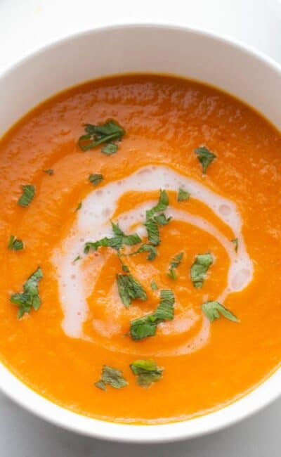 Two bowls of carrot ginger soup with a drizzle of coconut milk and a garnish of fresh parsley.