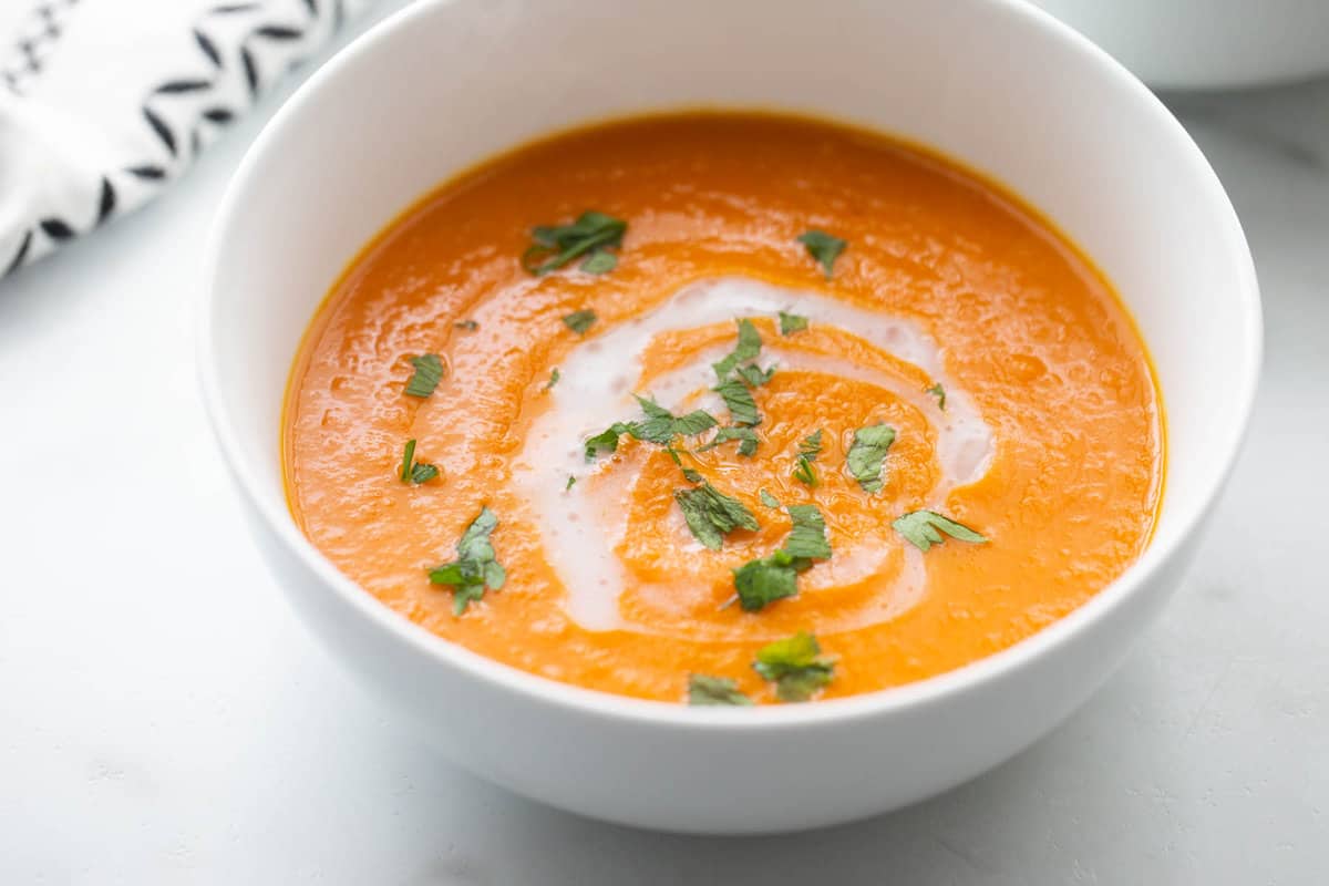 A bowl of carrot ginger soup with a drizzle of coconut milk and fresh herbs. 