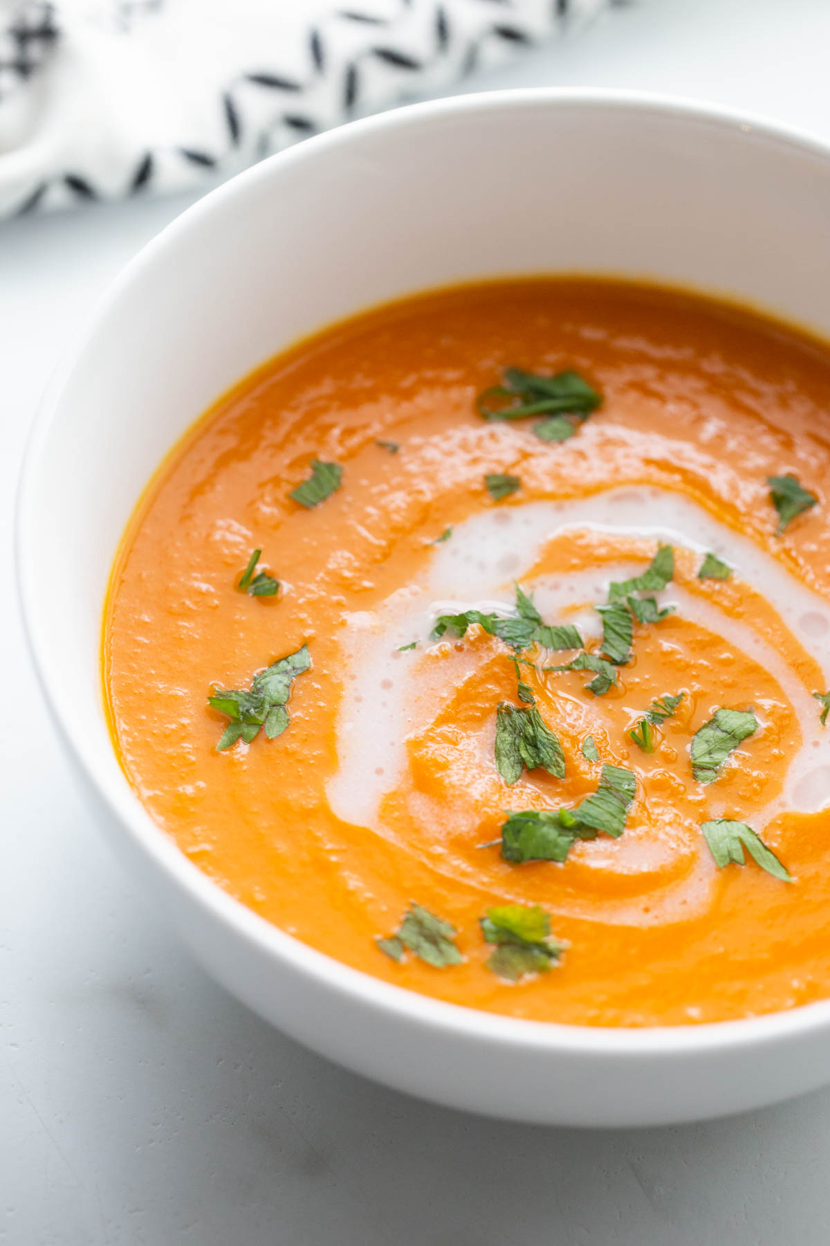 Close up photo of carrot ginger soup in a white bowl with a swirl of coconut milk and garnished with parsley.
