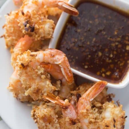A plate of gluten free coconut shrimp sitting next to some sweet chili sauce.