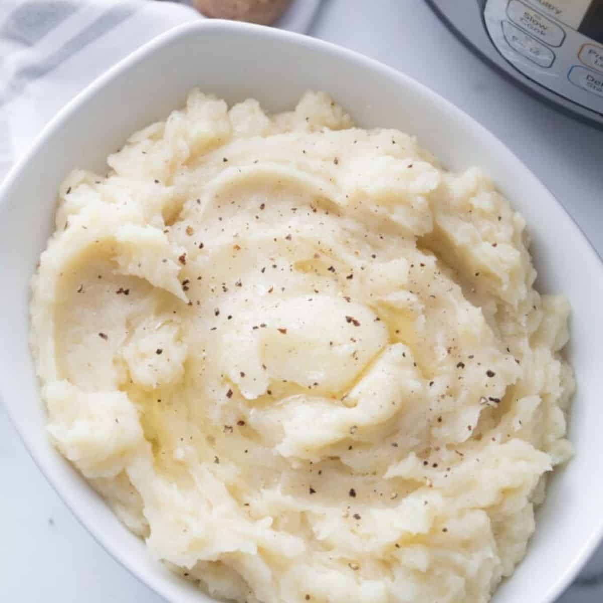 White serving bowl full of mashed potatoes topped with fresh black pepper and melted vegan butter making them dairy free.