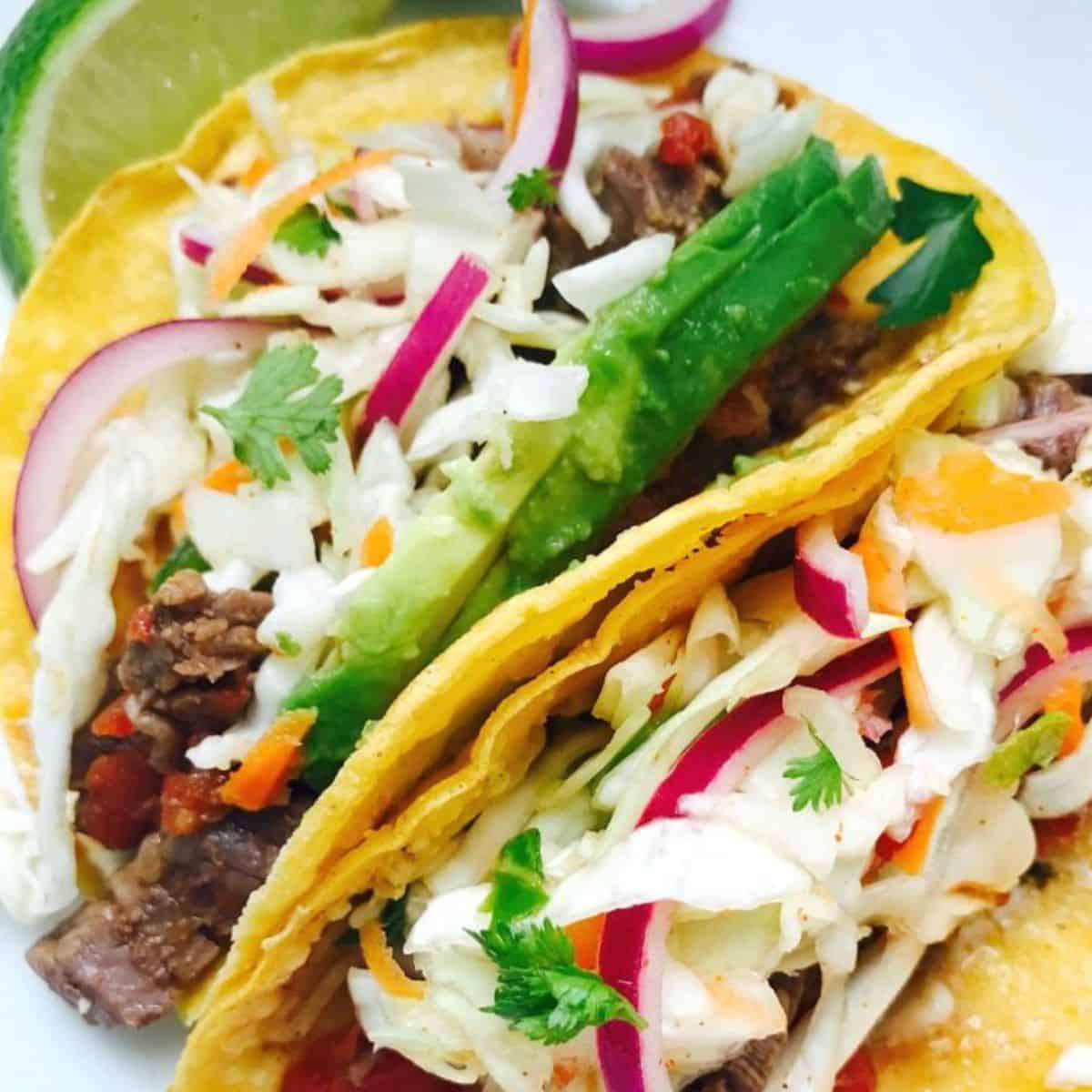 Close up of two flank steak tacos with cilantro lime slaw in corn tortillas.