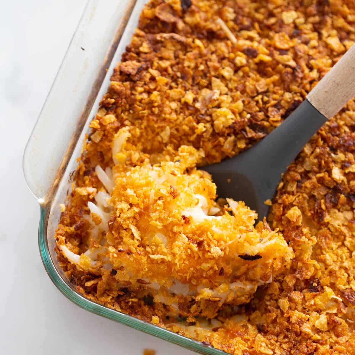 A pan of lightened up funeral potatoes with a serving spoon.