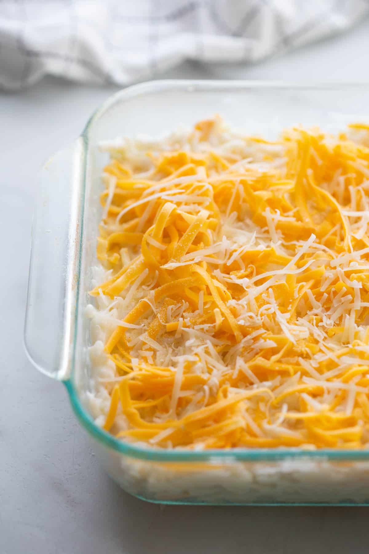 Shredded cheddar and parmesan cheese on top of cheesy hashbrown casserole