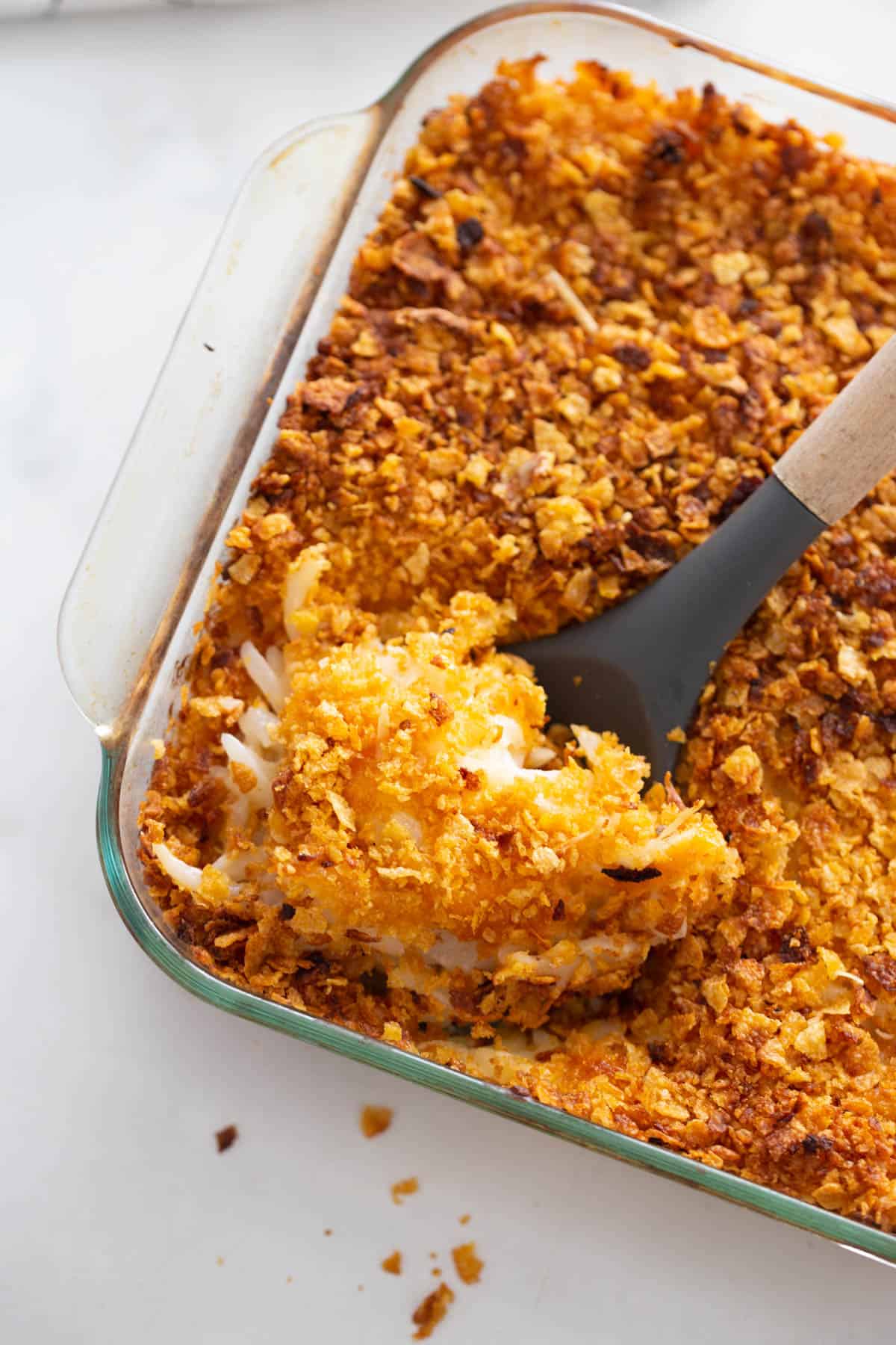 A pan of lightened up funeral potatoes with a serving spoon.