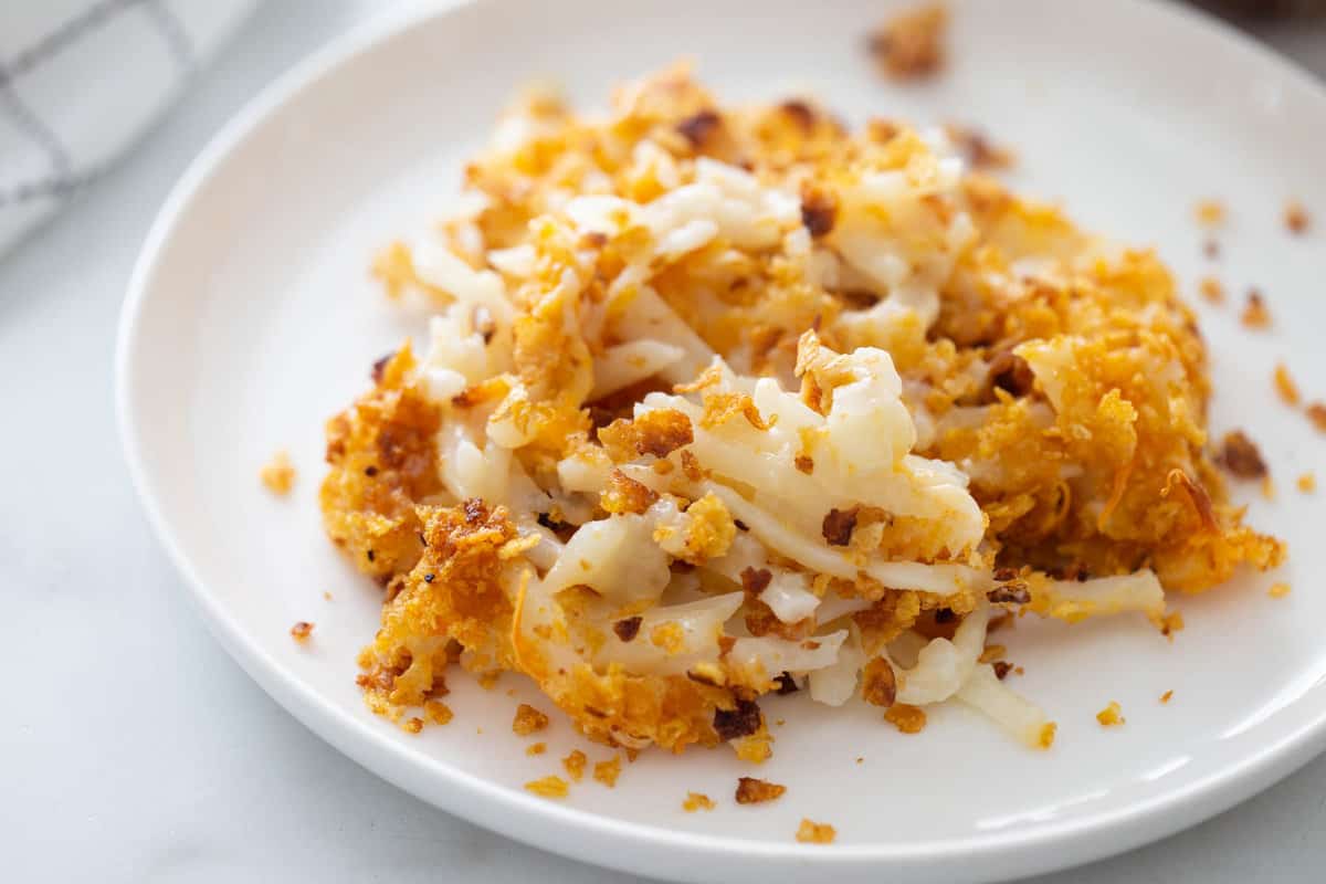 A white plate with cheesy hash brown casserole topped with cornflakes.