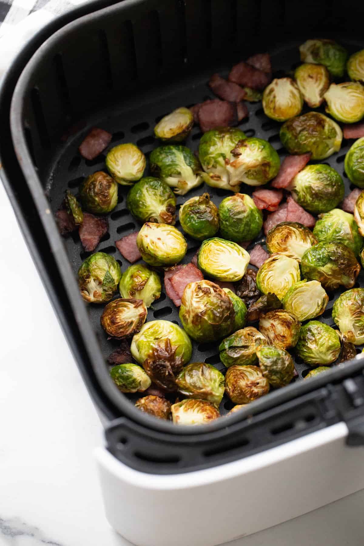 Air fryer basket with crispy Brussels sprouts and turkey bacon.